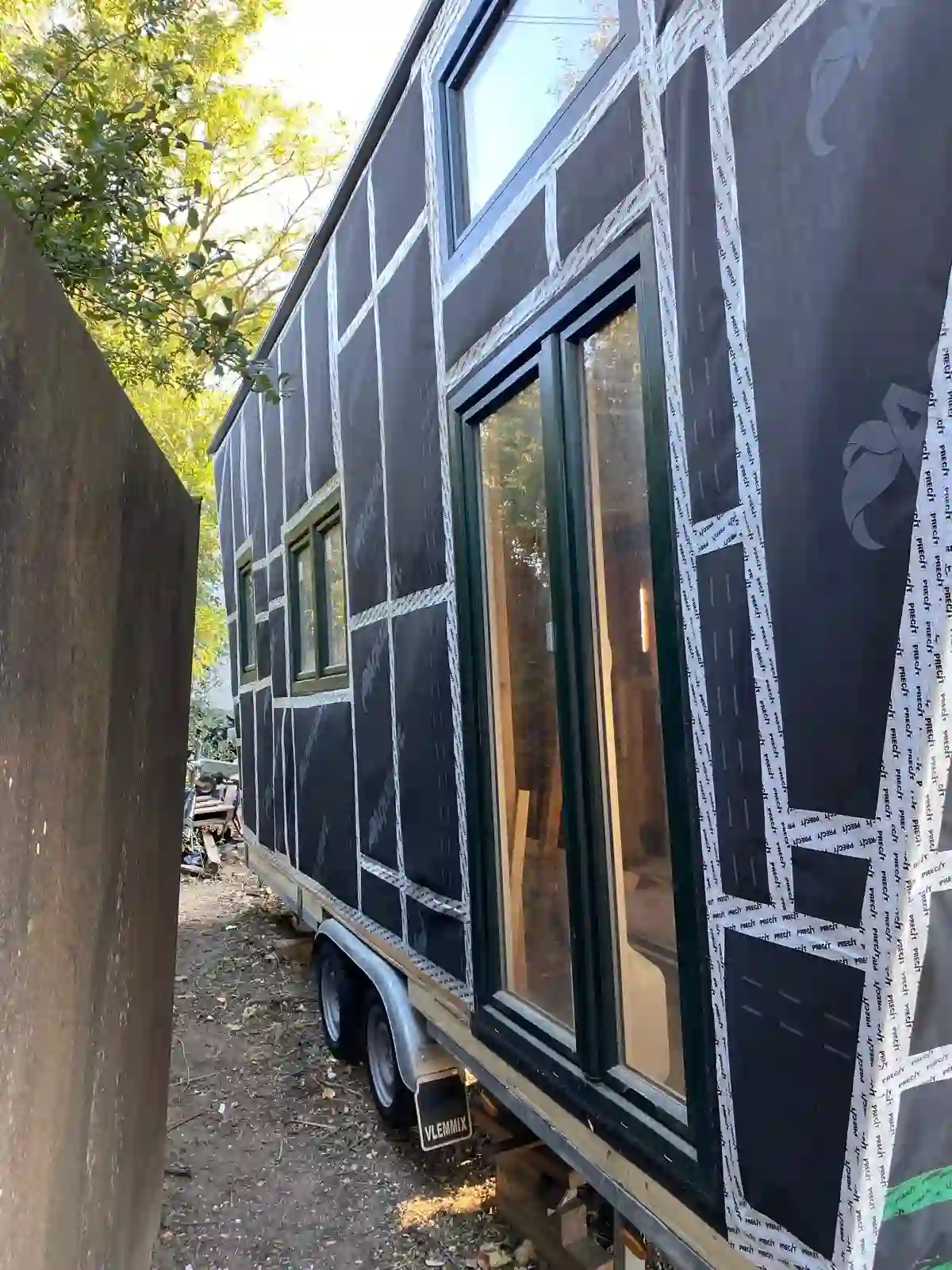 Die Außenhülle des Tiny Hauses mit abgeklebter Fassadenbahn und eingebauten Fenstern auf dem Anhänger